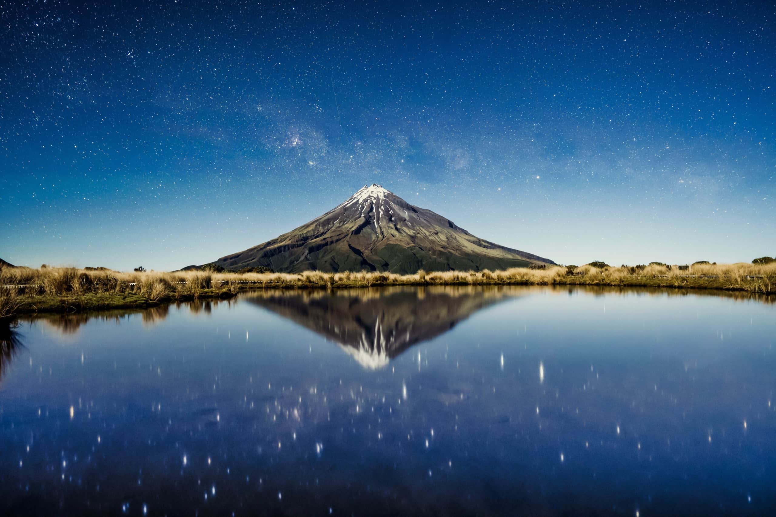 Mount Taranaki under a starlit sky, reflected in still water.